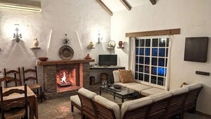 A cozy living room with a stone fireplace, wooden furniture, and a television. - Casa Zahora - extended families' first choice! (Cádiz)