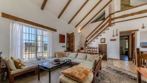 A spacious living room with a high ceiling, wooden beams, a large window, a staircase, and a stone floor. - Casa Zahora - extended families' first choice! (Cádiz)