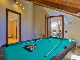 A pool table with balls, a ceiling light fixture, and a view of a balcony with a table and chairs.