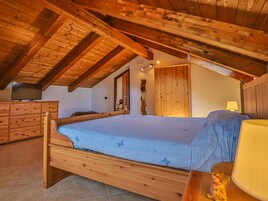A wooden bed in a room with a sloped ceiling and a wooden wardrobe.