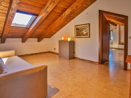 Una habitación con techo de madera inclinado, tragaluz, sofá, armario y un cuadro en la pared.