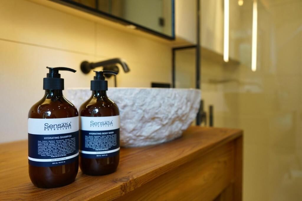 To flasker Sensatia Botanical Hydrating Shampoo og Body Wash på en træbordplade i et badeværelse.