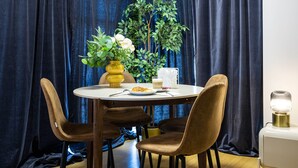 Un comedor con una mesa redonda, cuatro sillas, un florero con flores, una planta y una lámpara de mesa.