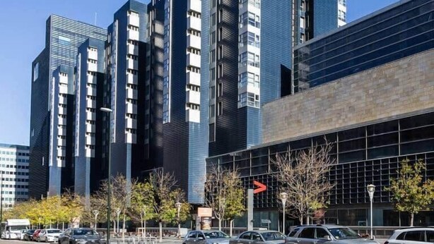 Un edificio moderno de varios pisos, con amplias ventanas y un estacionamiento con coches.