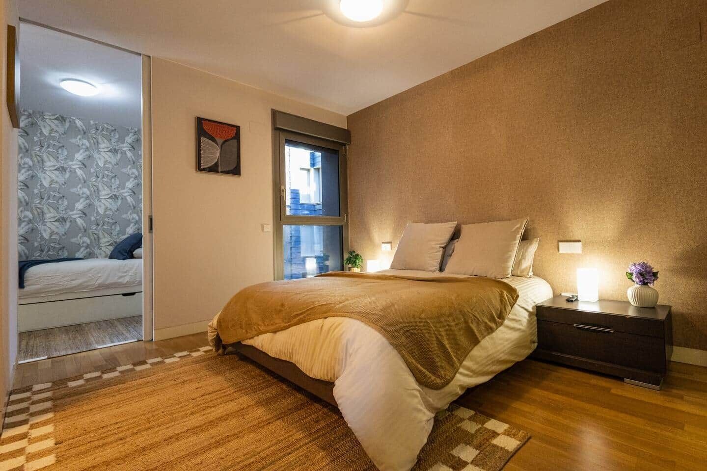 Une chambre à coucher avec un lit, une table de chevet, une lampe et une fenêtre.