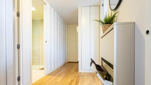 Un pasillo con suelo de madera, paredes blancas y un mueble blanco con una planta encima.