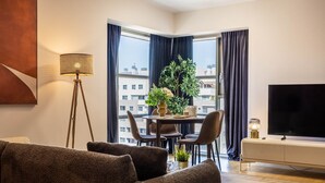 Una sala de estar moderna con un sofá, una mesa de comedor con sillas, un televisor y un ventanal con cortinas.