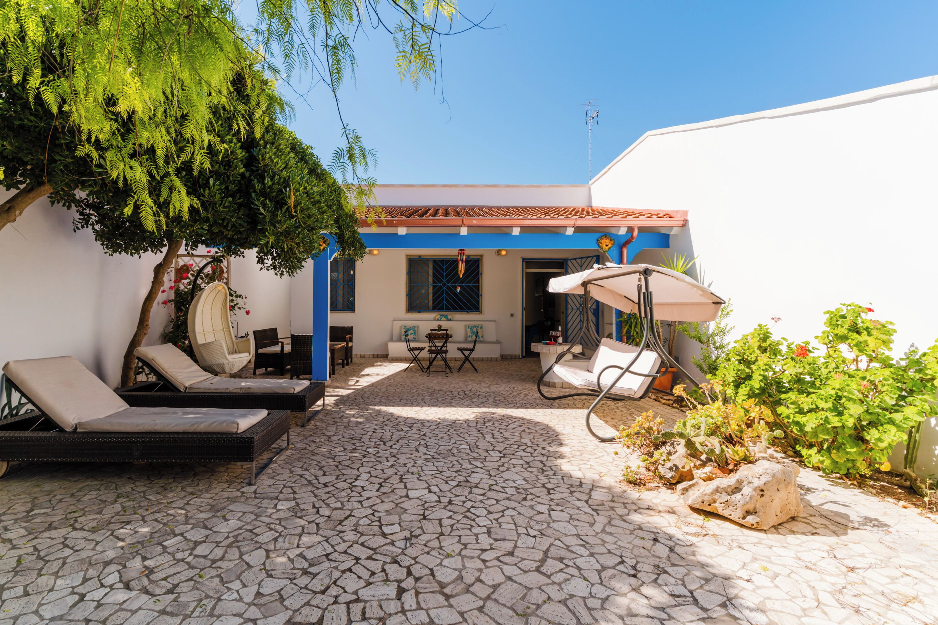 A courtyard with lounge chairs, a table, and a white wall with blue trim.