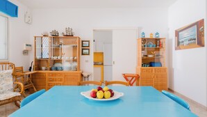 Ruokailutila, jossa on sininen pöytä, rottingista valmistetut tuolit ja hedelmäkulho.