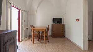 A room with a wooden dining table and chairs, a television on a cabinet, and a stove. - Villa Jole - Trilocale by BarbarHouse (Torre Suda)