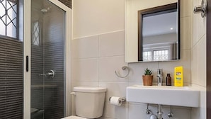 Ein modernes Badezimmer mit einer gläsernen Dusche, einer Toilette, einer kleinen Mülleimer und einem Waschbecken mit Spiegel darüber.