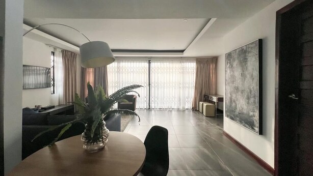 Ein modernes Wohnzimmer mit Essbereich, ausgestattet mit einem runden Tisch, Stühlen, einem Topf mit Pflanze, einem großen abstrakten Gemälde und einem Sofa.