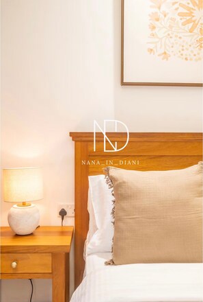 A neatly made bed with a wooden headboard, a bedside lamp, and a wall-mounted power outlet. - Nana in Diani’s Luxurious Escape 2bed Ac/wifi beachfront access (Diani Beach)