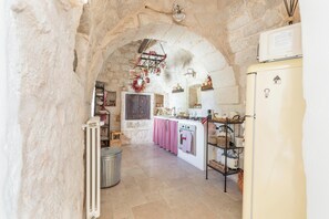A rustic kitchen with stone walls, a central archway, a white refrigerator, and a wooden cabinet. - Trulli Claudia by Perle di Puglia (Martina Franca)