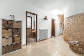 A spacious hallway with a stone wall, a large basket, and a white tiled floor. - Trulli Claudia by Perle di Puglia (Martina Franca)
