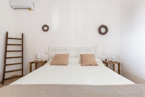 A bedroom with a bed, two nightstands, a wooden ladder, and two wall-mounted wreaths. - Trulli Claudia by Perle di Puglia (Martina Franca)