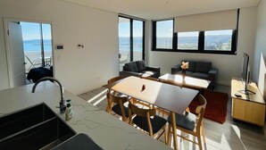 Une cuisine moderne dotée d’un grand îlot central, un coin repas avec une table et des chaises, et un espace de détente avec un canapé et un téléviseur.
