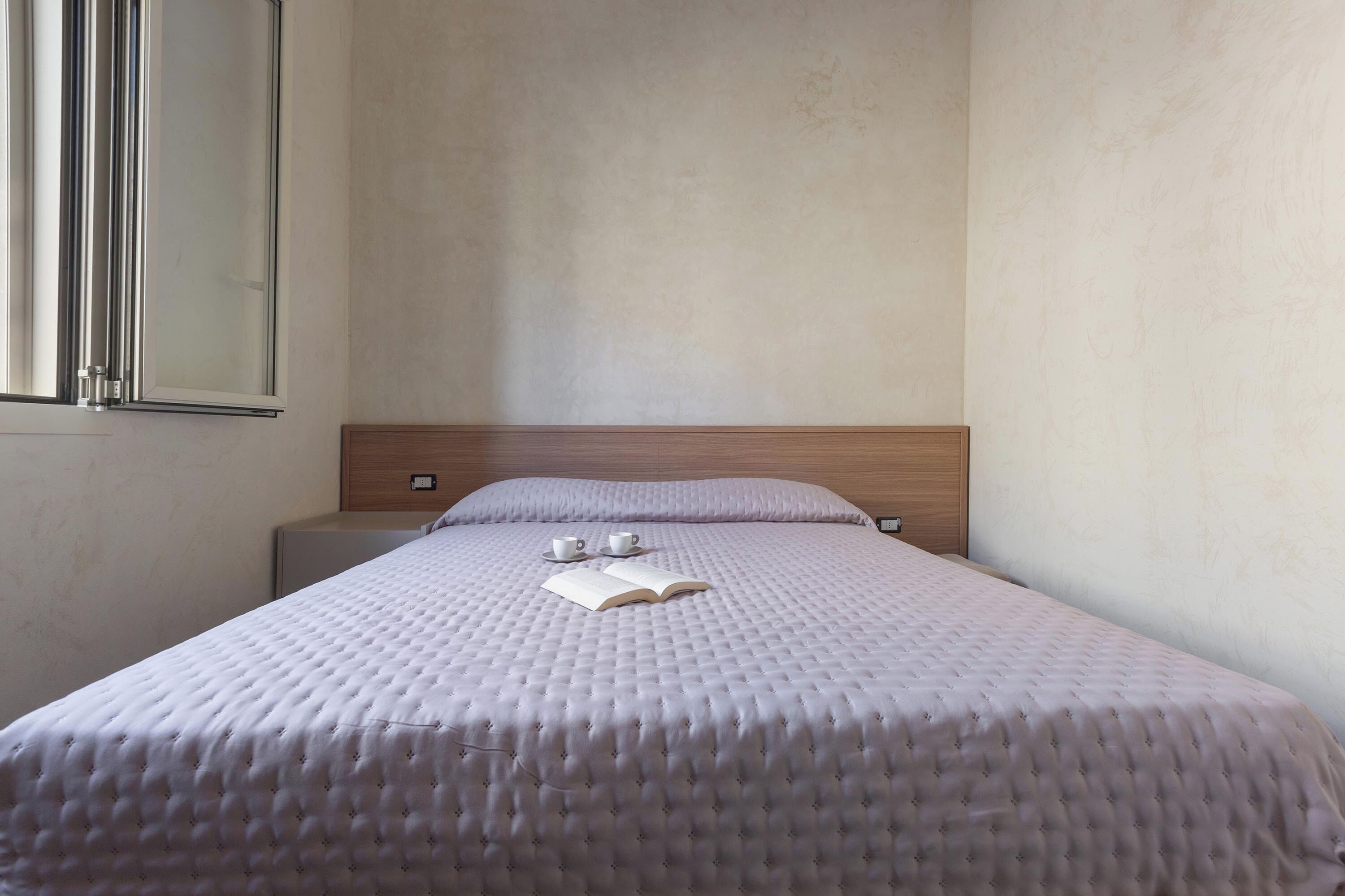A neatly made bed with a white duvet, a book, and two cups on the bed.