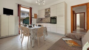 A modern kitchen with white cabinets, a dining table with chairs, and a sofa in the living area. - Villino Pascoli by BarbarHouse (Torre dell'Orso)