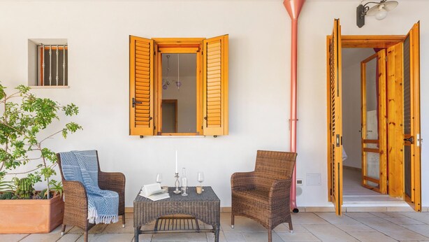 An outdoor seating area with wicker chairs, a table with a book and glasses, a potted plant, and a wooden door. - Villino Pascoli by BarbarHouse (Torre dell'Orso)