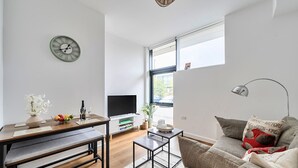 A modern living room with a TV, sofa, dining table, and a clock on the wall. - 2-Bed Staines Stay | Parking | Heathrow & London Access (Staines-upon-Thames)