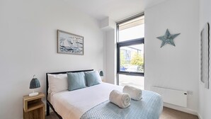 A bedroom with a bed, a nightstand, a window, and a star decoration. - 2-Bed Staines Stay | Parking | Heathrow & London Access (Staines-upon-Thames)