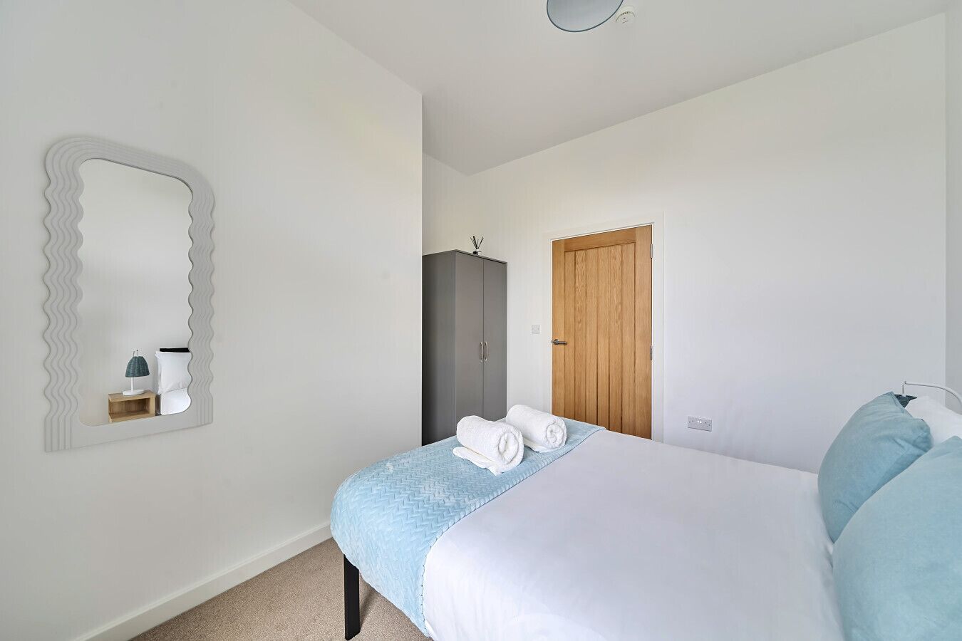 A bedroom with a bed, a wardrobe, a mirror, and a door.