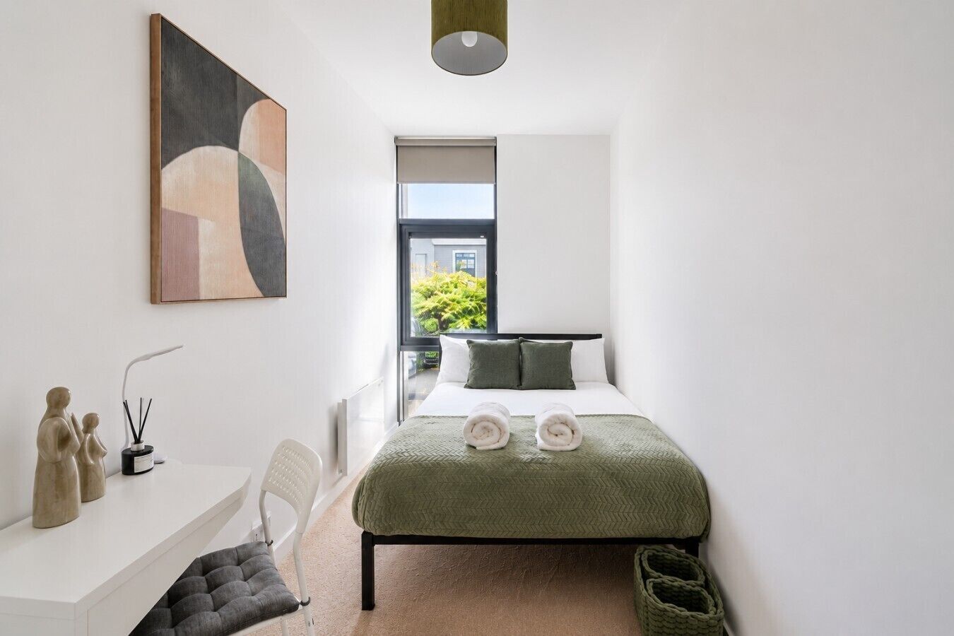A modern bedroom with a bed, a desk, and a window with a view of greenery.