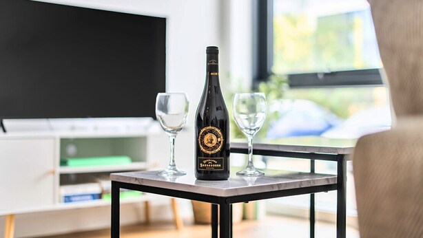 A bottle of wine on a table with two glasses, a TV, and a window with a view. - 2-Bed Staines Stay | Parking | Heathrow & London Access (Staines-upon-Thames)