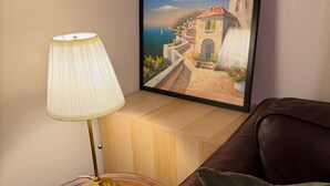 Ein Zimmer mit einem Holznachttisch, einer Lampe, einem gerahmten Gemälde mit Küstenansicht und einem braunen Ledersofa.