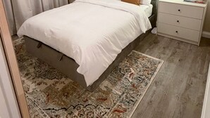 Ein Schlafzimmer mit Bett, Nachttisch, Lampe, Kleiderschrank und einem gemusterten Teppich.