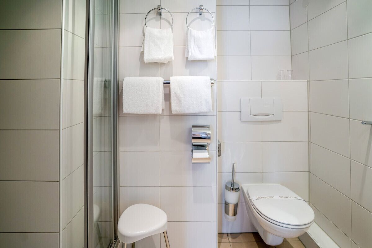 A modern bathroom with white tiles, a glass shower enclosure, a toilet, and a sink with a towel rack above.