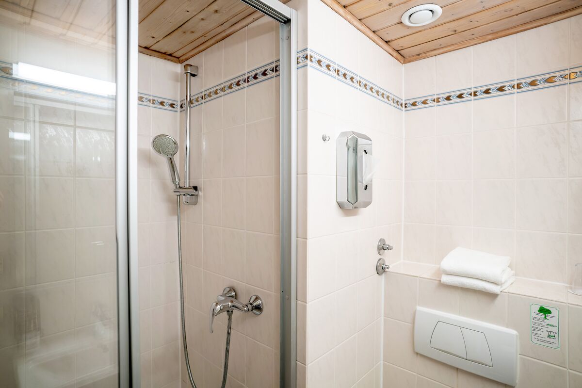 Un baño con cabina de ducha de vidrio, ducha de mano, dispensador de toallas en la pared y un perchero.