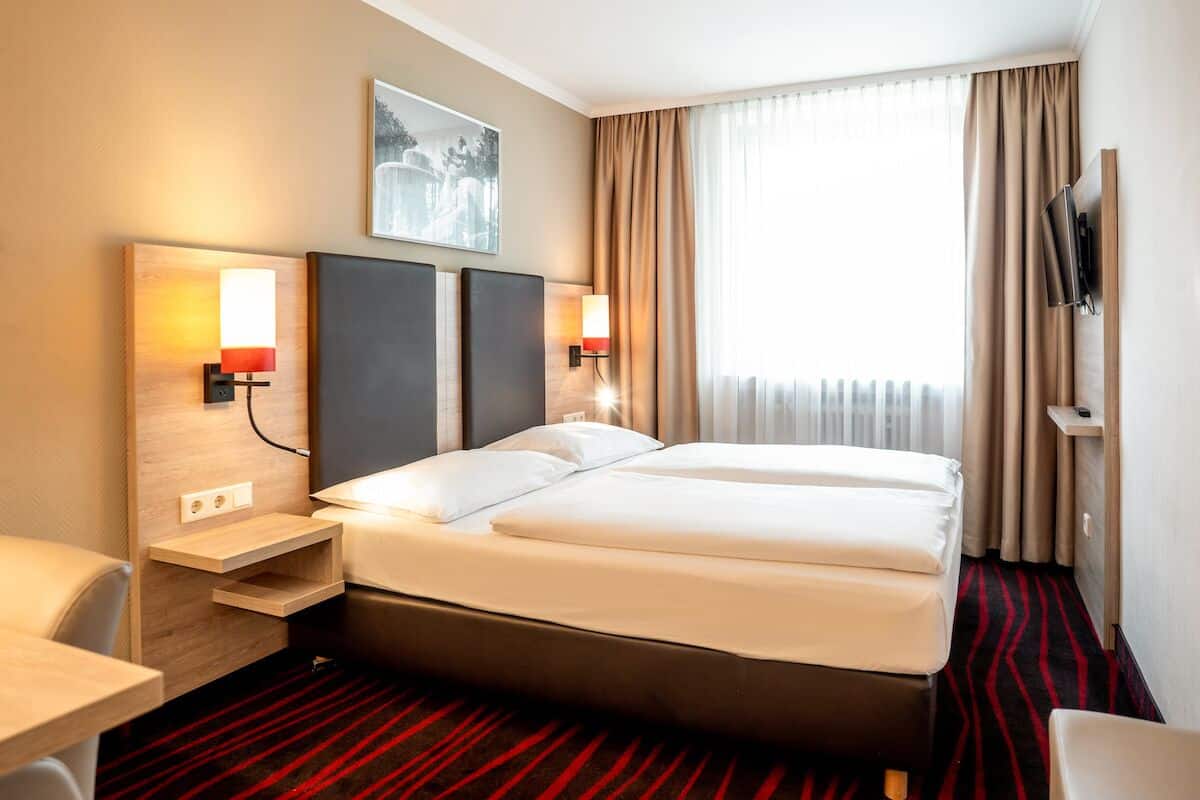 Ein Hotelzimmer mit einem großen Bett, zwei Nachttischen, einem Schreibtisch und einem an der Wand montierten Fernseher.