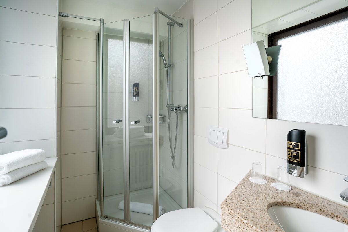 Un baño moderno con ducha acristalada, inodoro blanco y encimera de granito con lavabo y dispensador de jabón.