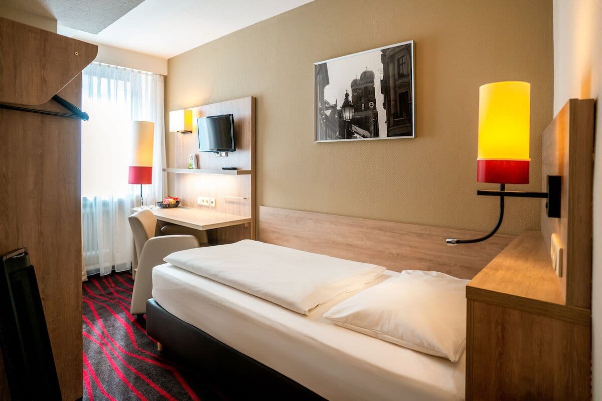 Ein Hotelzimmer mit Bett, Schreibtisch, Stuhl, Fernseher und Lampe.