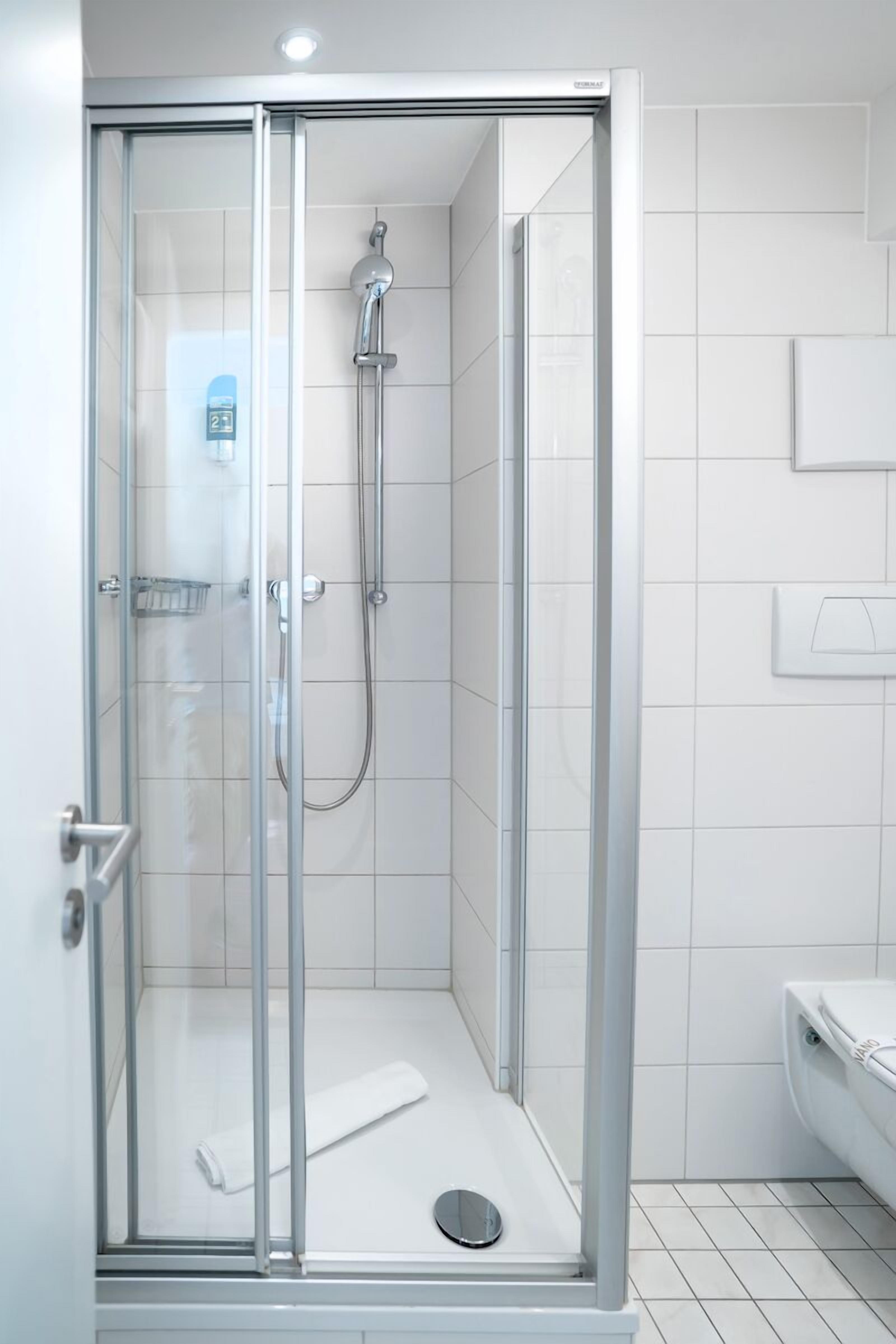 A modern bathroom with a glass-enclosed shower, white tiled walls, and a toilet.