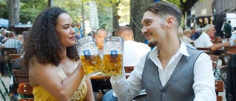 Dos personas brindando con vasos de cerveza en una mesa de comedor al aire libre.