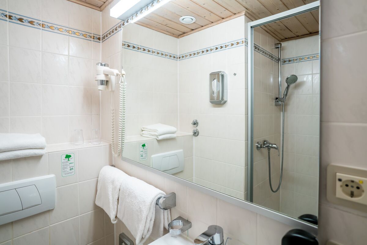 Un bagno con doccia, un water, un lavandino, uno specchio e un portasciugamani.