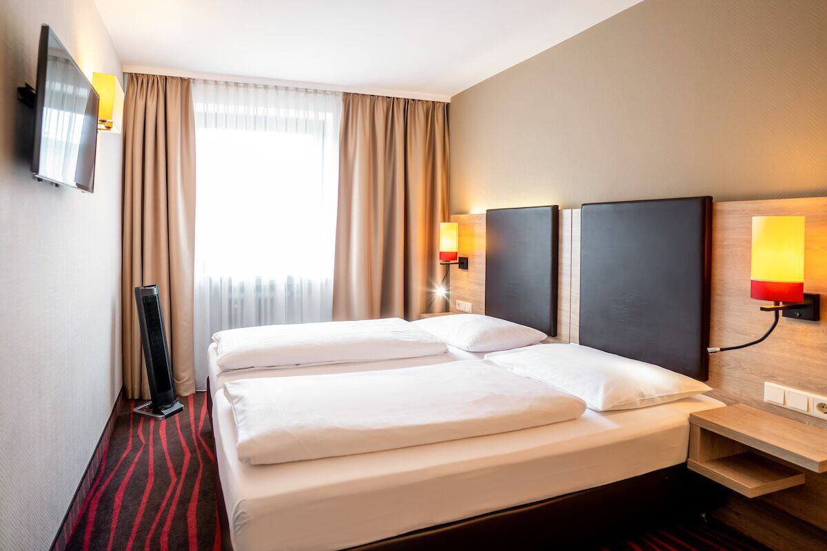 Ein Hotelzimmer mit zwei Betten, einem Flachbildfernseher, einem Heizlüfter und Wandleuchten.