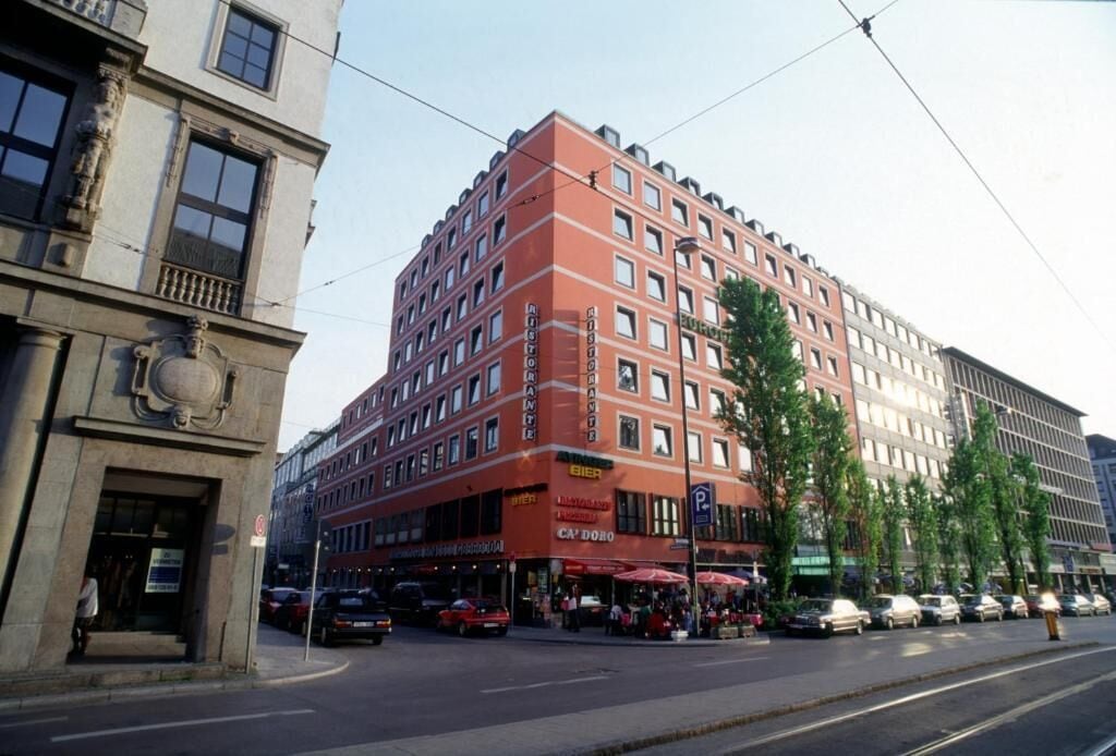 Un hotel de varios pisos con fachada roja, múltiples balcones y un restaurante en la planta baja.