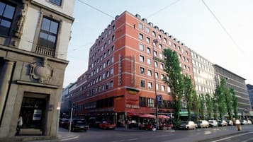 A multi-story hotel with a red facade, multiple balconies, and a ground-level restaurant.