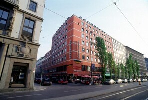A multi-story hotel with a red facade, multiple balconies, and a ground-level restaurant.