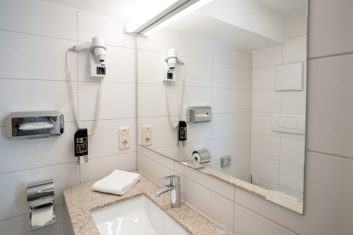 Un baño moderno con lavabo, espejo, dispensador de toallas y secador de pelo.