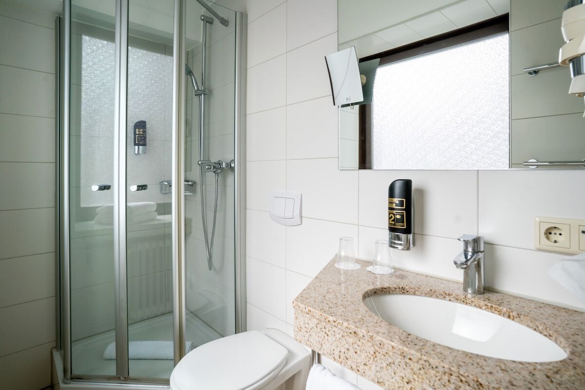 Un baño moderno con ducha de vidrio, inodoro blanco y lavamanos con encimera de granito.