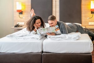 A hotel room with a bed, a nightstand, and a wall-mounted lamp.