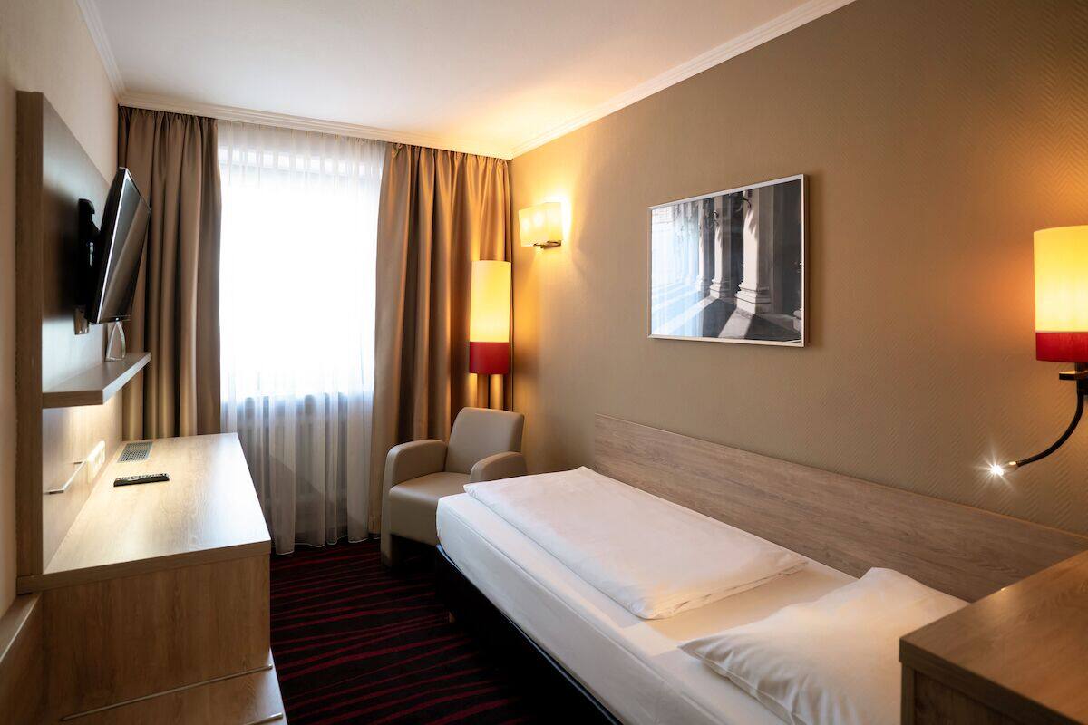 Ein Hotelzimmer mit Bett, Schreibtisch, Stuhl, Fernseher und zwei Wandlampen.