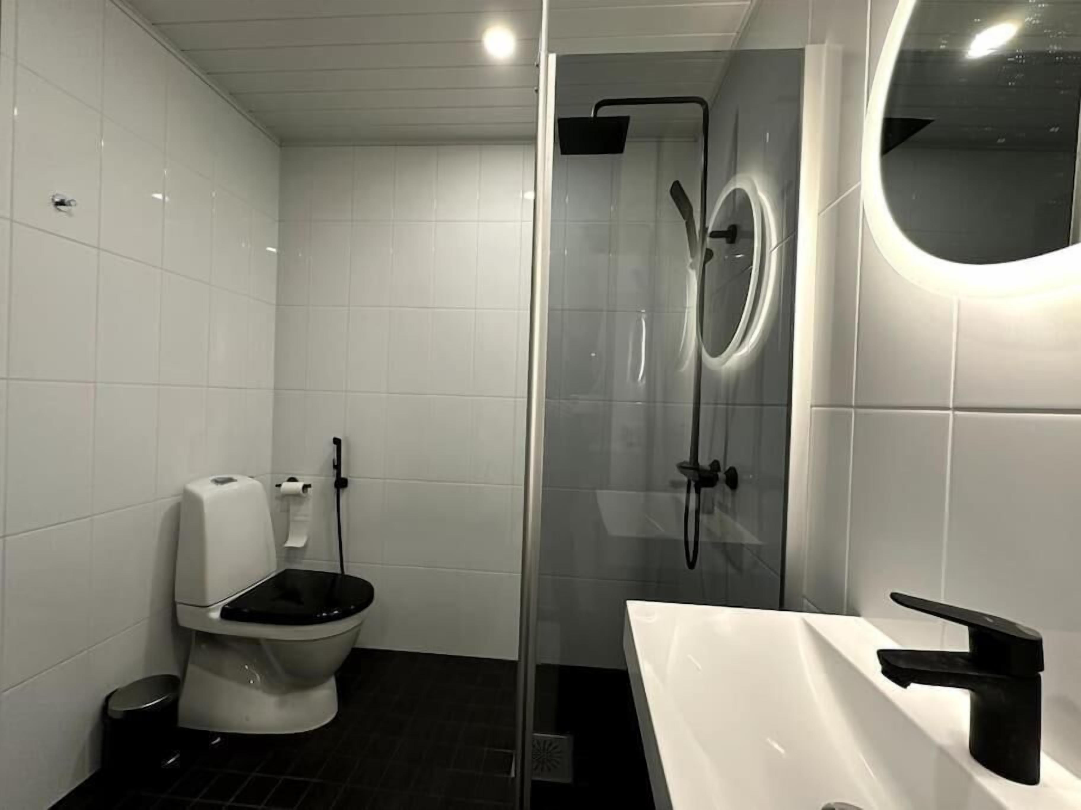Een moderne badkamer met toilet, een douchecabine en een witte wastafel met zwarte kraan.
