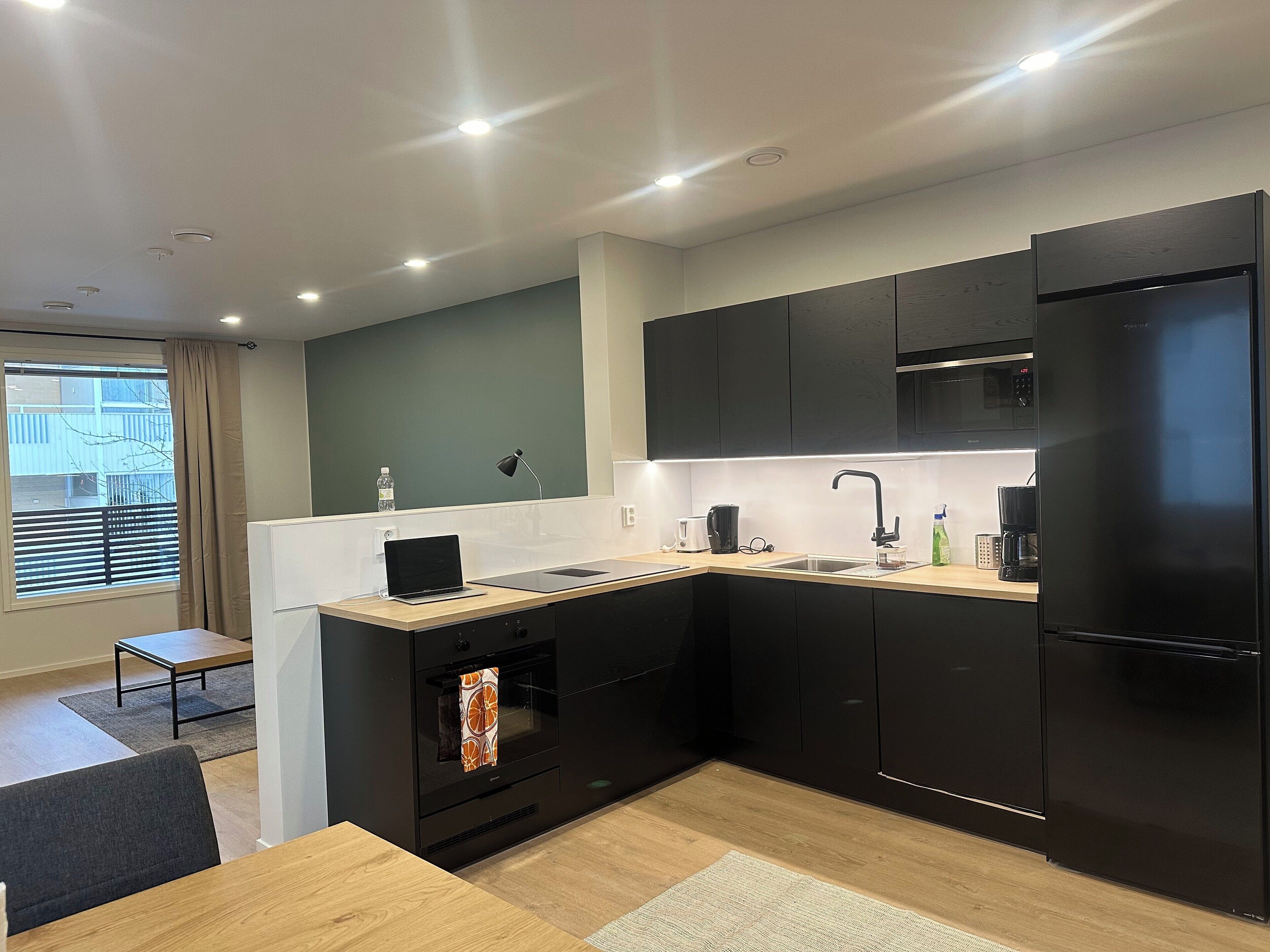 Une cuisine moderne avec des meubles de couleur noire, un réfrigérateur en acier inoxydable et une table à manger en bois.
