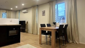 Un salon moderne comprenant un coin repas, un téléviseur et une grande fenêtre avec des rideaux.